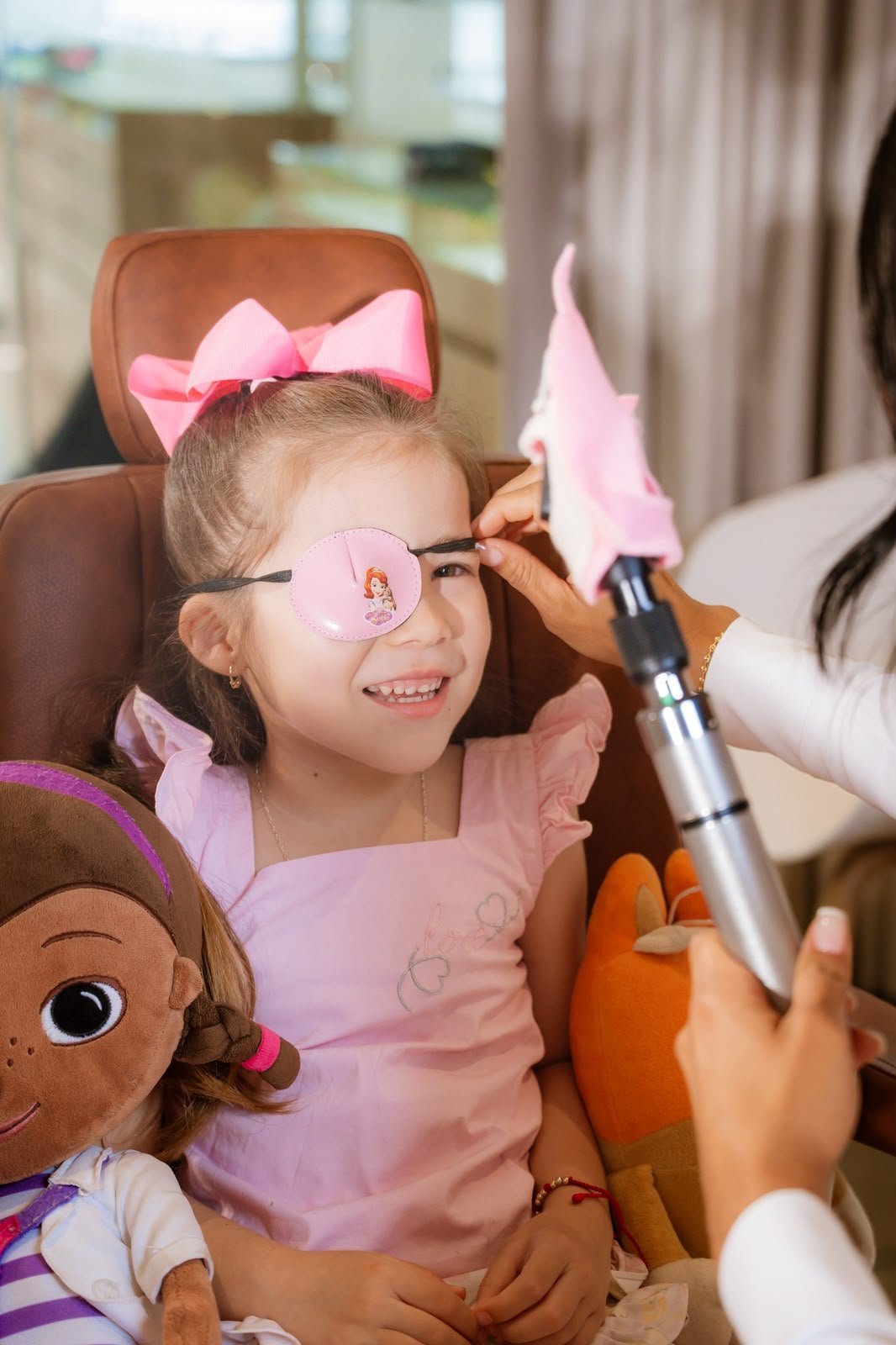 Niña sonriendo mientras le colocan un parche oclusivo rosa con motivo de Sofía durante una consulta de optometría pediátrica en el consultorio